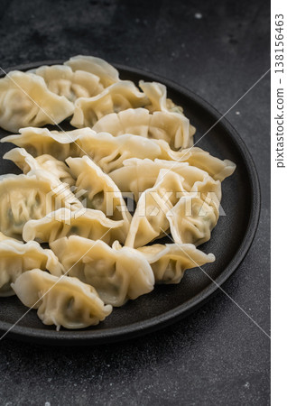 Tasty steamed gyoza wontons arranged on a black plate over concrete background. Authentic asian appetizer for menus and culinary projects. Tasty steamed gyoza wontons arranged on a black plate over concrete background. Authentic asian appetizer for menus and culinary projects. 138156463