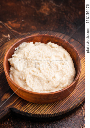 Overhead shot of rich white condiment (aioli or horseradish) in a bowl on a dark textured wood surface. Gourmet serving style. Overhead shot of rich white condiment (aioli or horseradish) in a bowl on a dark textured wood surface. Gourmet serving style. 138156476