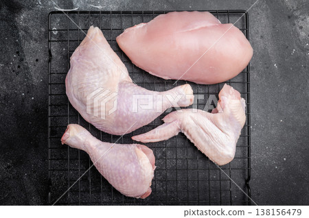 Assortment of fresh raw chicken meat on a metal rack over a textured black surface. High angle view with generous copy space. 138156479