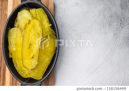 Rustic pickled cucumber slices in cast iron dish with garlic and spices on textured light background, vibrant brined yellow food. Rustic pickled cucumber slices in cast iron dish with garlic and spices on textured light background, vibrant brined yellow food. 138156499
