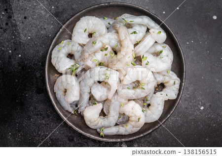 Raw peeled shrimp with thyme in a dark metal plate on a textured black background. Maximum contrast with copy space. Raw peeled shrimp with thyme in a dark metal plate on a textured black background. Maximum contrast with copy space. 138156515