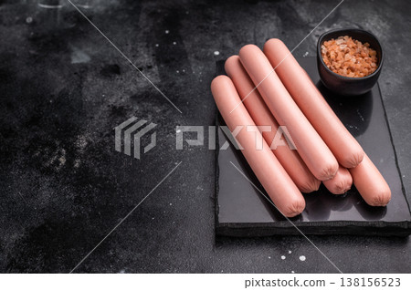 Four raw pink hot dog sausages (frankfurters/wieners) on a contrasting dark stone background with Himalayan salt. Copy space. Four raw pink hot dog sausages (frankfurters/wieners) on a contrasting dark stone background with Himalayan salt. Copy space. 138156523