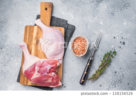 Uncooked duck legs laid out on a wooden chopping board, enhanced by a touch of thyme and Himalayan salt, against a modern gray background 138156526
