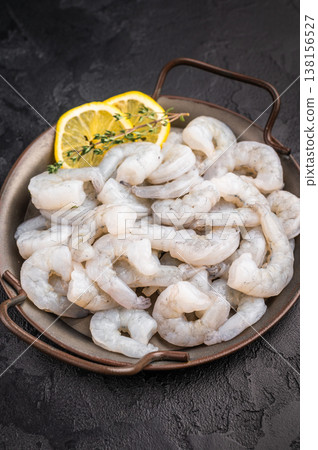 Raw peeled shrimp prawn with lemon and thyme in a metal pan on a textured black background. Maximum contrast with copy space. Raw peeled shrimp prawn with lemon and thyme in a metal pan on a textured black background. Maximum contrast with copy space. 138156527