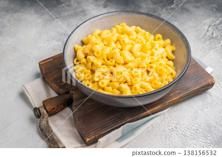 Savory mac and cheese served in a stylish bowl. Wooden board and gray background create a cozy, modern food scene. Savory mac and cheese served in a stylish bowl. Wooden board and gray background create a cozy, modern food scene. 138156532