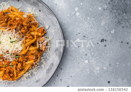 Hearty Italian bolognese pasta topped with minced meat sauce and grated cheese on a gray ceramic plate against stone background. 138156542