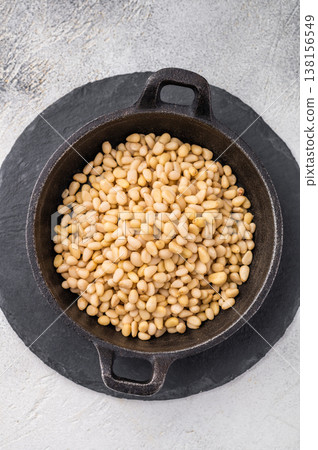 Raw pine nuts arranged in a small cast iron dish on a slate plate over a light textured surface creating a clean contrast for recipe and food visuals Raw pine nuts arranged in a small cast iron dish on a slate plate over a light textured surface creating a clean contrast for recipe and food visuals 138156549
