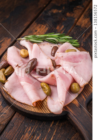 Cured pork slices lonza with olives and rosemary on a rustic wooden board over dark aged wood creating a simple and commercial food background. 138156572