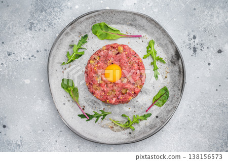 Fresh steak tartare with herbs on modern plate against textured concrete surface ideal for fine dining visuals culinary ads and recipe concepts. Fresh steak tartare with herbs on modern plate against textured concrete surface ideal for fine dining visuals culinary ads and recipe concepts. 138156573