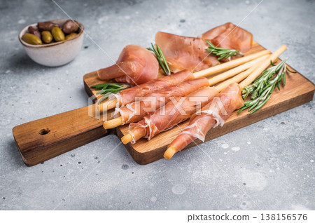 Gourmet Italian Antipasto with prosciutto crudo, grissini breadsticks, and olives on a rustic wooden board. Top view with copy space. Gourmet Italian Antipasto with prosciutto crudo, grissini breadsticks, and olives on a rustic wooden board. Top view with copy space. 138156576