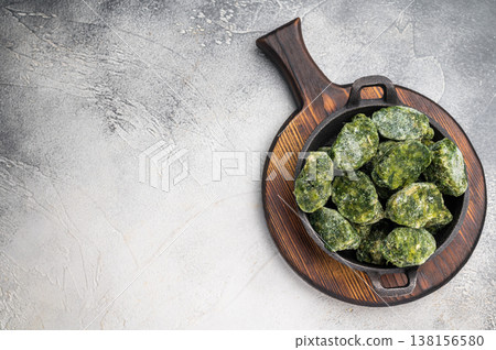 Overhead shot of frozen spinach blocks in a cast iron skillet on a wooden board. Grey textured background with copy space. Overhead shot of frozen spinach blocks in a cast iron skillet on a wooden board. Grey textured background with copy space. 138156580