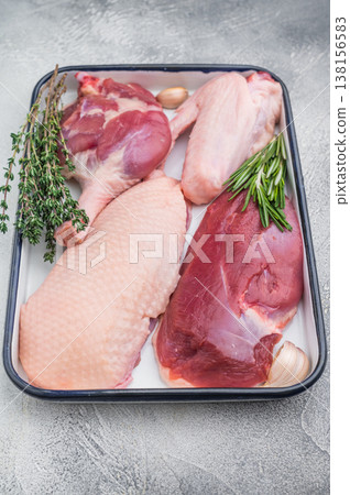 Raw duck parts breast wing thigh and fillet with herbs and garlic in enamel tray on light stone background with vintage fork for food stock images. 138156583