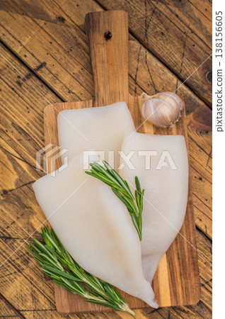 Raw calamari and fresh rosemary on vintage wood board captured for culinary design seafood menus and Mediterranean style visuals 138156605