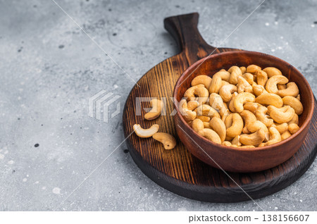 Cashew nuts in a wooden bowl placed on a rustic board against a textured grey background creating a warm natural food scene for culinary stock Cashew nuts in a wooden bowl placed on a rustic board against a textured grey background creating a warm natural food scene for culinary stock 138156607