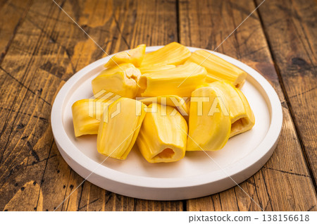 Sweet, golden yellow jackfruit pods (bulbs) served on a white plate on a rustic wooden table. Fresh, tropical fruit snack. 138156618