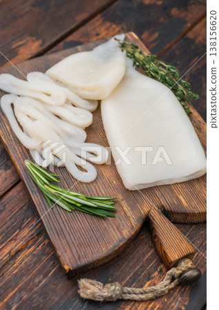Cleaned squid fillets and rings on textured wood board with rosemary and garlic perfect seafood setup for culinary themes. Cleaned squid fillets and rings on textured wood board with rosemary and garlic perfect seafood setup for culinary themes. 138156620