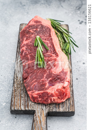 Premium New York steak raw and marbled with rosemary placed on rustic board on bright stone background great for gourmet cooking concepts Premium New York steak raw and marbled with rosemary placed on rustic board on bright stone background great for gourmet cooking concepts 138156621