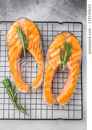 Two cooked salmon slices with herbs resting on a metal grid against a soft gray surface for fresh clean modern food styling. 138156623