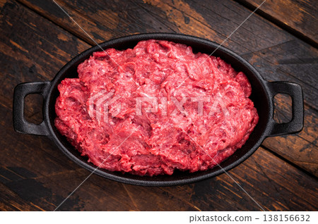 Raw ground wild game meat (venison/boar) in a black skillet on a rustic wooden board, seasoned with fresh thyme and peppercorns. 138156632