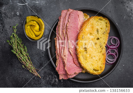 Gourmet pastrami brisket sandwich with seed bread, pickles and red onion rings on a dark stone background, deli meat closeup. 138156633