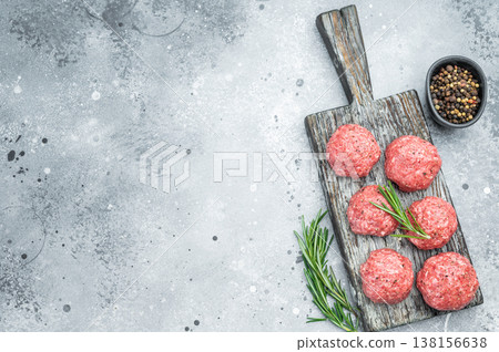 Fresh raw meatballs or frikkadel with rosemary and pepper on rustic wooden board over gray background ideal for cooking, protein and food prep themes. Fresh raw meatballs or frikkadel with rosemary and pepper on rustic wooden board over gray background ideal for cooking, protein and food prep themes. 138156638