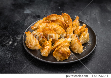 Golden potstickers fried dumplings mandu jiaozi on rustic dark surface Asian snack with crispy texture and sesame topping Golden potstickers fried dumplings mandu jiaozi on rustic dark surface Asian snack with crispy texture and sesame topping 138156651