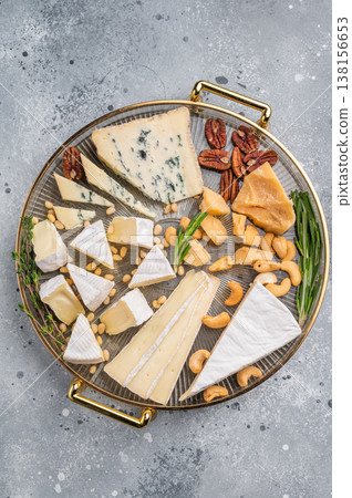 Elegant cheese platter with nuts and herbs presented on a gold tray against a modern gray concrete backdrop for a gourmet look. Elegant cheese platter with nuts and herbs presented on a gold tray against a modern gray concrete backdrop for a gourmet look. 138156653