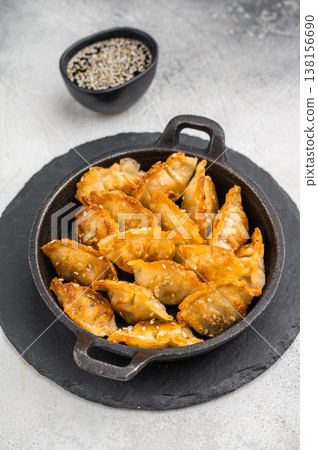 Golden fried dumplings jiaozi sprinkled with sesame served in black skillet on bright stone surface perfect Asian snack. 138156690