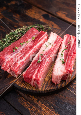 Raw beef short ribs with thyme and pink peppercorns on a dark wooden cutting board. Excellent for a BBQ recipe or restaurant menu. Raw beef short ribs with thyme and pink peppercorns on a dark wooden cutting board. Excellent for a BBQ recipe or restaurant menu. 138156695