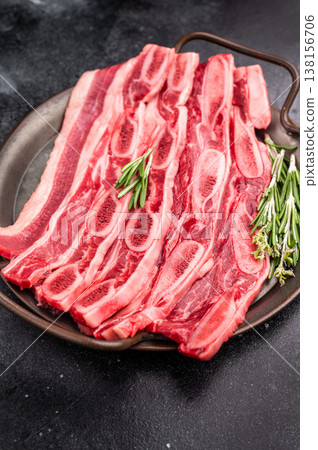 Raw Flanken cut beef short ribs (Kalbi) with rosemary and thyme on a dark, rustic background. Copy space. Raw Flanken cut beef short ribs (Kalbi) with rosemary and thyme on a dark, rustic background. Copy space. 138156706
