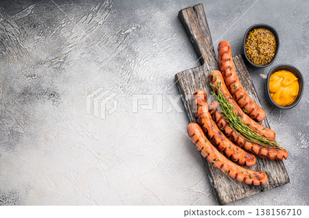 Grilled and cut sausages (wieners/frankfurters) on a rustic wooden board with two types of mustard. Perfect for BBQ menu design. 138156710