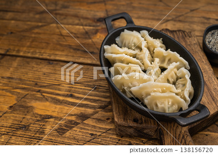 Boiled Asian dumplings potstickers sprinkled with sesame in black skillet on natural wood table authentic oriental cuisine. 138156720