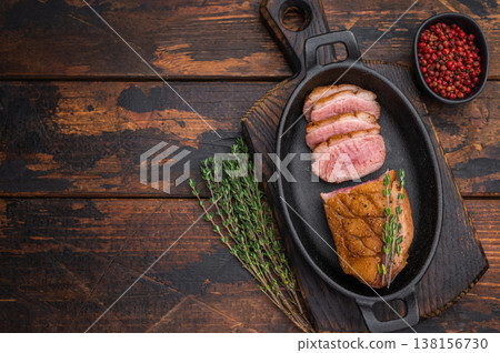 Seared duck breast sliced and served in cast-iron skillet with thyme on rustic wooden background ideal for gourmet food photography. 138156730