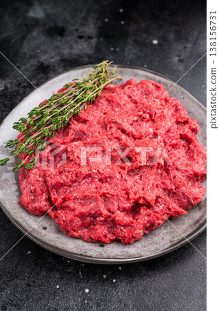 Raw ground wild game meat rabbit hare on a textured grey plate with fresh thyme, set on a dark, moody stone background. 138156731