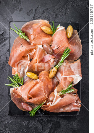 Appetizer of Sliced Ham and Olives garnished with rosemary, set on a dark rustic surface. Traditional Mediterranean snack. Appetizer of Sliced Ham and Olives garnished with rosemary, set on a dark rustic surface. Traditional Mediterranean snack. 138156737