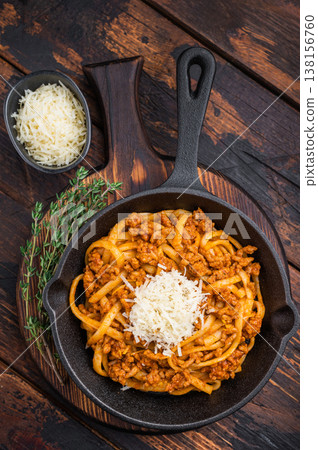 Rustic pasta bolognese with rich meat ragu and parmesan served in a cast iron skillet on dark wooden background with fresh thyme. Rustic pasta bolognese with rich meat ragu and parmesan served in a cast iron skillet on dark wooden background with fresh thyme. 138156760
