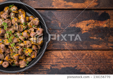 Tasty chicken offal stew in cast iron pan on dark wooden surface great for restaurant advertising or food blogs. Tasty chicken offal stew in cast iron pan on dark wooden surface great for restaurant advertising or food blogs. 138156770