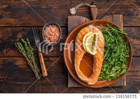 A wholesome grilled salmon portion paired with zesty citrus and vibrant greens arranged on a brown plate against rich wooden tones for hearty food imagery. A wholesome grilled salmon portion paired with zesty citrus and vibrant greens arranged on a brown plate against rich wooden tones for hearty food imagery. 138156775