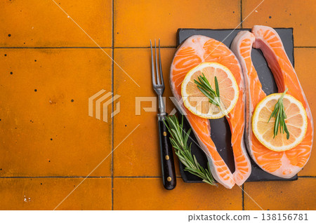 Fresh raw sea trout steaks with lemon and rosemary arranged on a dark slate board over a warm terracotta tile background perfect for premium food visuals. 138156781