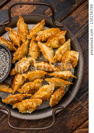 Golden crunchy gyoza dumplings served with sesame sauce on a textured light surface. Asian fried potstickers top view. Golden crunchy gyoza dumplings served with sesame sauce on a textured light surface. Asian fried potstickers top view. 138156789