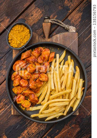 German currywurst with fries on a black plate over rustic wooden background perfect for street food visuals and fast food stock images. German currywurst with fries on a black plate over rustic wooden background perfect for street food visuals and fast food stock images. 138156793