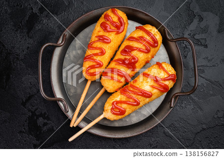 Golden corn dogs with ketchup topping served on plate with sauce, crunchy fast food snack on dark background Golden corn dogs with ketchup topping served on plate with sauce, crunchy fast food snack on dark background 138156827