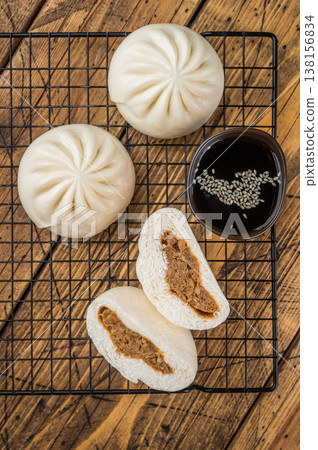 Asian steamed buns with meat filling cut open and served with dipping sauce, soft fluffy bao bread on wooden background 138156834