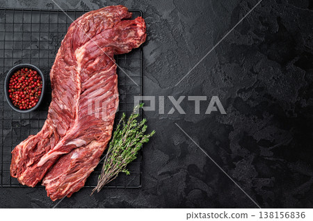 Closeup raw onglet hanger steak on metal grate over black textured surface, rich red meat with visible fibers and fat, ideal for barbecue and cooking Closeup raw onglet hanger steak on metal grate over black textured surface, rich red meat with visible fibers and fat, ideal for barbecue and cooking 138156836