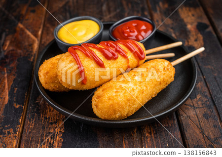 Golden corn dogs with ketchup topping served on plate with sauce, crunchy fast food snack on dark background Golden corn dogs with ketchup topping served on plate with sauce, crunchy fast food snack on dark background 138156843