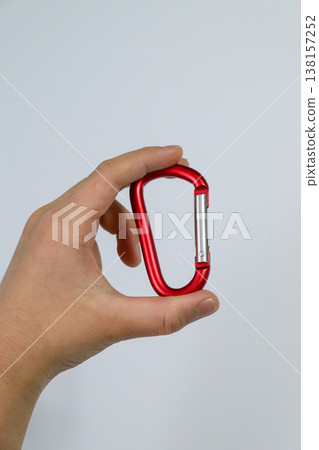 一手拿著紅色登山扣，背景是白色。 138157252