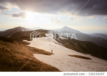 Snow covered ridge leading toward distant mountain peaks under golden light 138158297