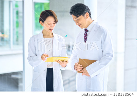 一名身穿白大褂的日本男醫生和一名身穿白大褂的日本女醫生正在審閱文件並進行會診。 一名身穿白大褂的日本男醫生和一名身穿白大褂的日本女醫生正在審閱文件並進行會診。 138158504