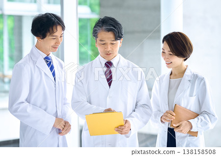 身穿白大褂的醫生和醫療團隊一邊審閱文件一邊討論。 身穿白大褂的醫生和醫療團隊一邊審閱文件一邊討論。 138158508