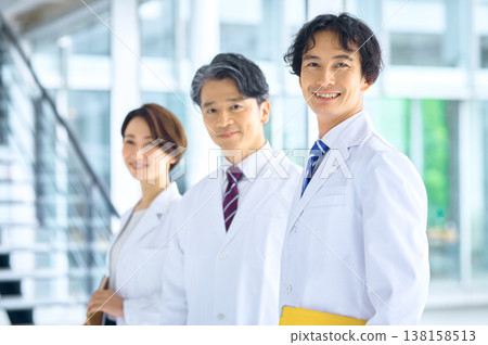A team of Japanese doctors and medical staff smile in the brightly lit hospital lobby. A team of Japanese doctors and medical staff smile in the brightly lit hospital lobby. 138158513